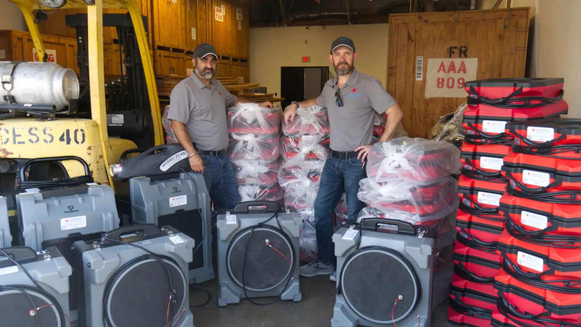 Unified Restoration LLC co-founders standing with professional-grade air movers, dehumidifiers, and restoration equipment in their Chandler, Arizona facility