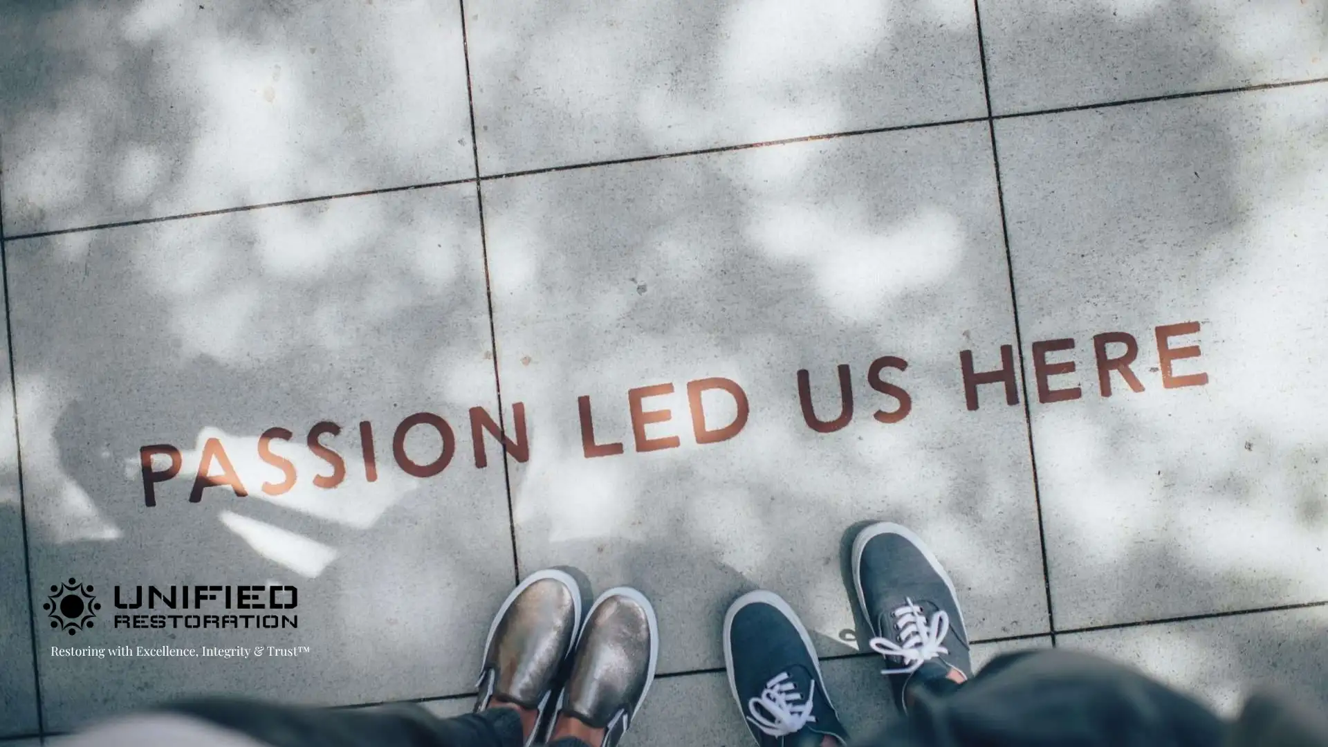 Overhead view of two people standing together on concrete pavers engraved with "PASSION LED US HERE" in copper lettering — representing the founding story and shared vision behind Unified Restoration LLC, a family-owned restoration company in Mesa, Arizona