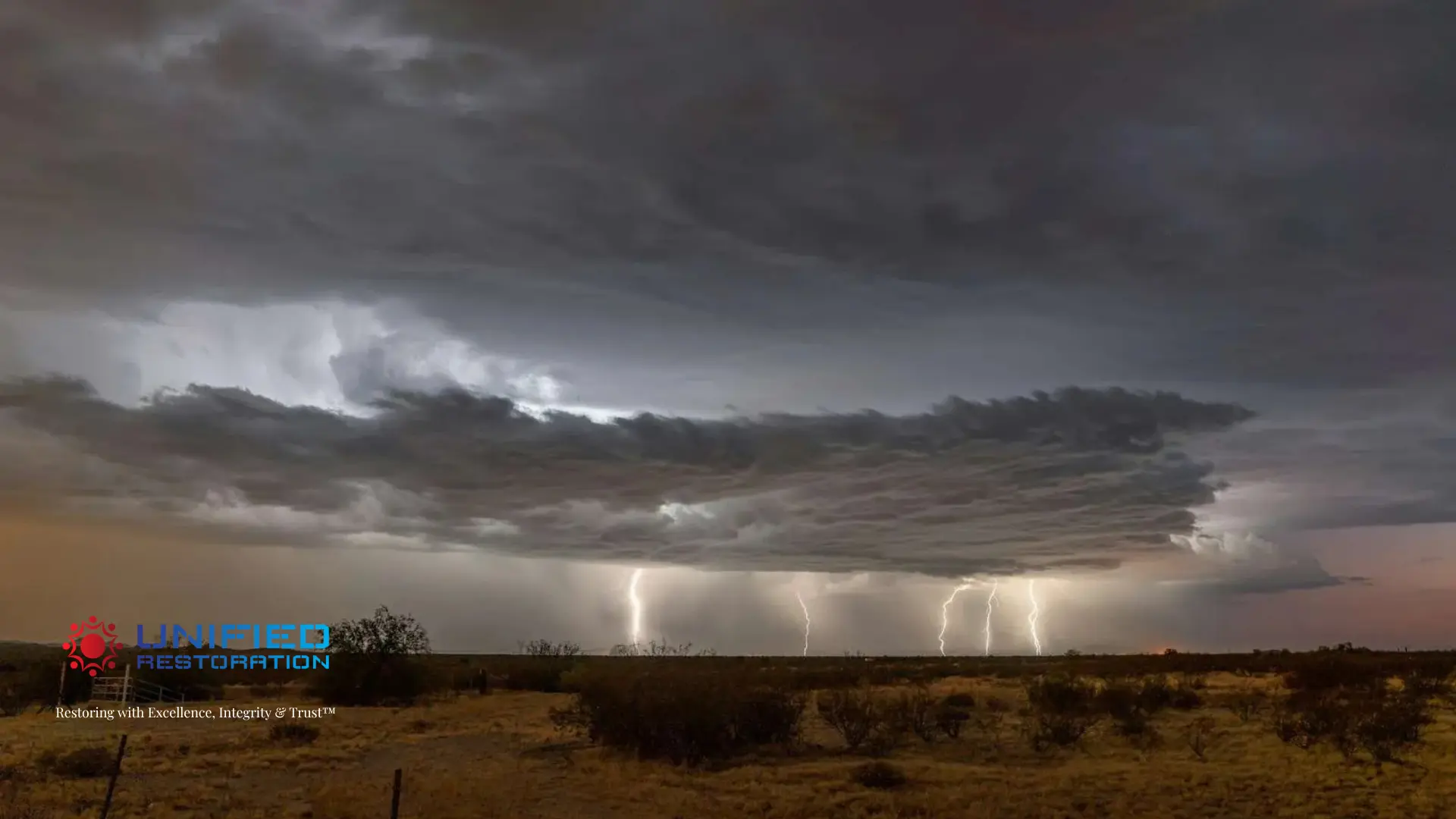 Dramatic Arizona monsoon supercell with five simultaneous lightning strikes over a flat desert landscape at dusk — amber haboob dust haze on the left, clearing pink sky on the right — monsoon preparedness and water damage risk for Phoenix Metro homeowners by Unified Restoration LLC